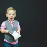 boy wearing gray vest and pink dress shirt holding book