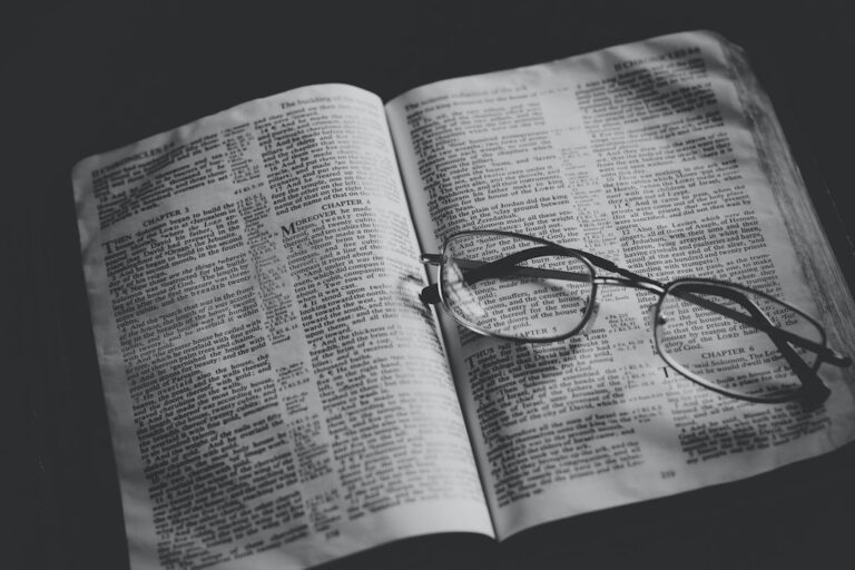 grayscale photo of eyeglasses on top of book