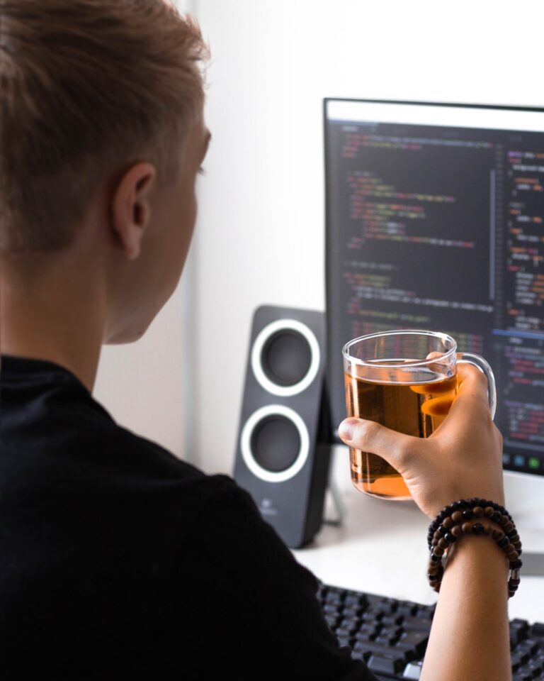 man holding clear glass mug while facing flat screen monitor