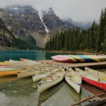 photo of assorted-color canoes on body of water surrounded by pine trees